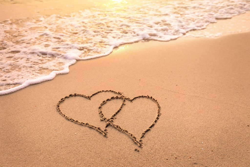 Romantic honeymoon holiday or Valentine's day on the beach concept with two hearts drawn on the sand, tropical getaway for couples, love symbol